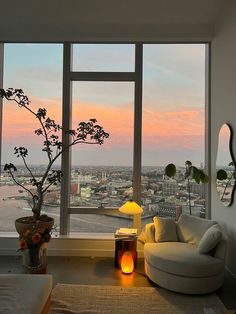 a living room filled with furniture and a large window overlooking the city at sunset or dawn