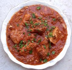 a white bowl filled with meat and tomato sauce on top of a marble countertop