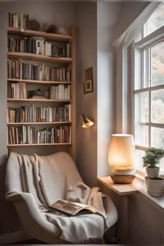 a white chair sitting in front of a window next to a book shelf filled with books