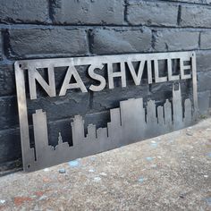 a metal sign with the name nashville on it next to a brick wall in front of a building