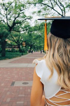 a woman wearing a graduation cap and gown looking at the trees in front of her