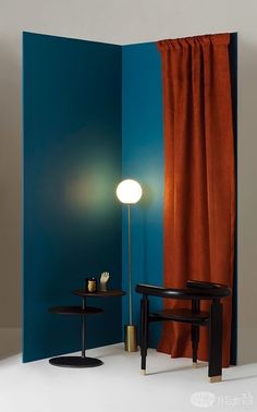 a room with two chairs and a table in front of a blue wall, next to an orange drapes