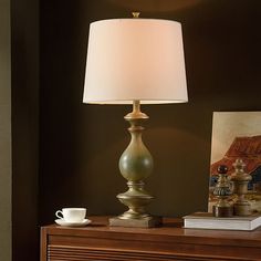 a lamp is on top of a dresser next to a coffee cup and bookcase