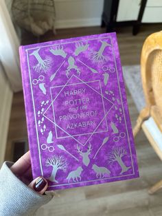 a person holding up a purple book with the words harry potter and her symbols on it