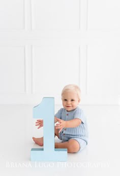 a baby is sitting on the floor next to a blue number one sign that says 1