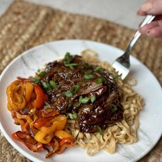 a white plate topped with noodles and meat next to a fork on top of a table