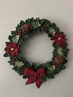 a crocheted wreath hanging on the wall with pine cones and poinsettis