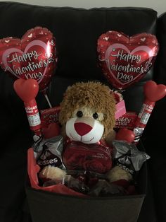 a teddy bear sitting in a basket filled with valentine's day candy and balloons