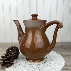 a brown vase sitting on top of a white doily next to a pine cone