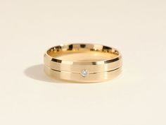 a yellow gold wedding band with a diamond set in the center, on a white background