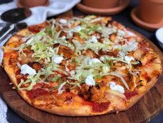 a pizza sitting on top of a wooden plate covered in cheese and veggies