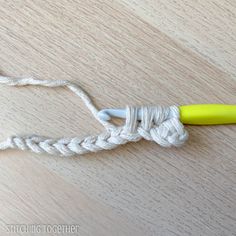 a yellow crochet hook on a wooden table next to a white rope with an orange handle