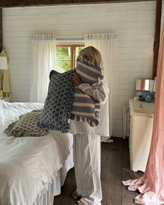 a woman standing in front of a bed with pillows on it's back and her arms wrapped around the pillow