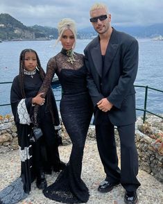 a man and two women standing next to each other in front of a body of water