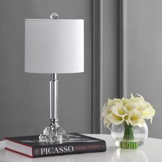 a table with a lamp and a book on it next to a vase with flowers