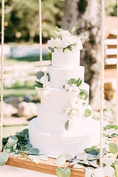 a white wedding cake sitting on top of a wooden table with greenery around it