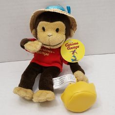 a stuffed monkey wearing a red shirt and hat with a yellow rubber duck toy in front of it