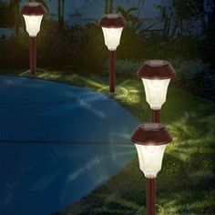 three lights that are in the grass near each other on a path at night time