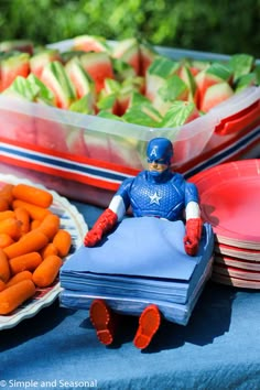 a table topped with plates and bowls filled with veggies next to a captain america figure