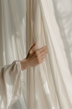 a person's hand reaching out from behind a curtain to touch the sheer fabric