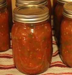 several jars filled with different kinds of food on top of a red and white table cloth