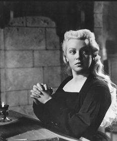 a black and white photo of a woman sitting at a table with her hands clasped