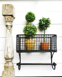 three potted plants are sitting in a wire basket on a shelf next to a pillar