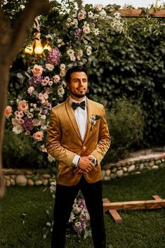 a man in a tuxedo standing next to a flower arch