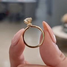 a woman's hand holding a gold ring with a diamond on it