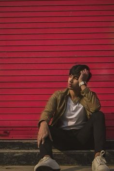 a man sitting against a red wall talking on a cell phone