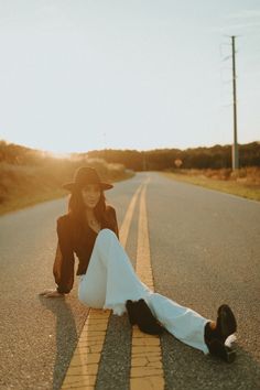 a woman laying on the side of an empty road with her legs spread out and wearing a hat