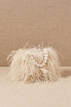 a white purse with pearls and feathers on the front, sitting against a beige background