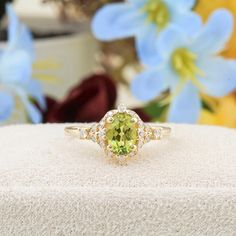 an oval cut peridot and diamond ring on top of a white box with flowers in the background