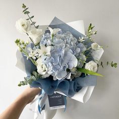 a bouquet of blue and white flowers is being held by a person's hand