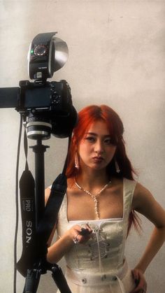 a woman standing in front of a camera with her hand on the tripod,