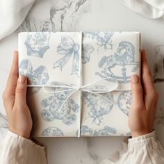 two hands holding a gift wrapped in blue and white wrapping paper with bows on it