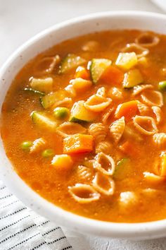 a white bowl filled with pasta and veggies soup on top of a table