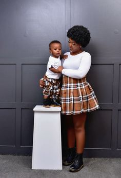 a woman holding a baby standing next to a wall