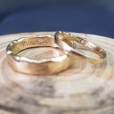 two gold wedding rings sitting on top of a piece of wood with the word love written on it