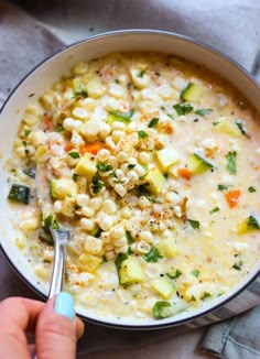 a person holding a spoon in a bowl filled with corn and veggie soup