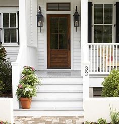 an image of a white house with black shutters and potted plants on the front porch