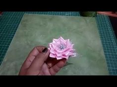 a person holding a pink flower on top of a green table next to a cutting board