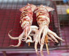 octopus skewers are being grilled on a metal rack with toothpicks