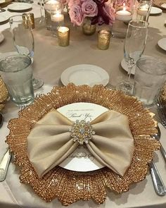 the table is set with silver and gold place settings, napkins, and flowers