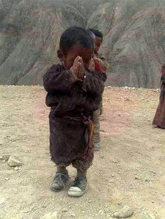 two young boys standing in the dirt with their hands together and one is covering his face