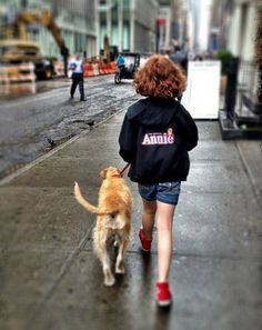 a woman walking her dog down the street in the rain with an annie shirt on