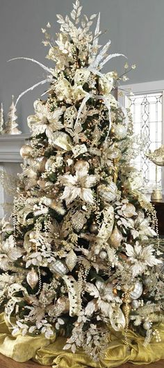 a white christmas tree in a living room decorated with gold and silver ornaments, surrounded by other holiday decorations