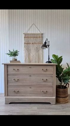 a dresser with two potted plants and a macrame hanging on the wall