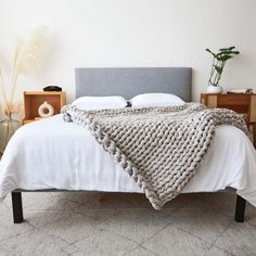 a bed with a blanket on top of it next to two nightstands and a potted plant