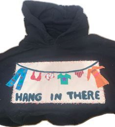 a black hoodie that says hang in there with clothes hanging from it's sides